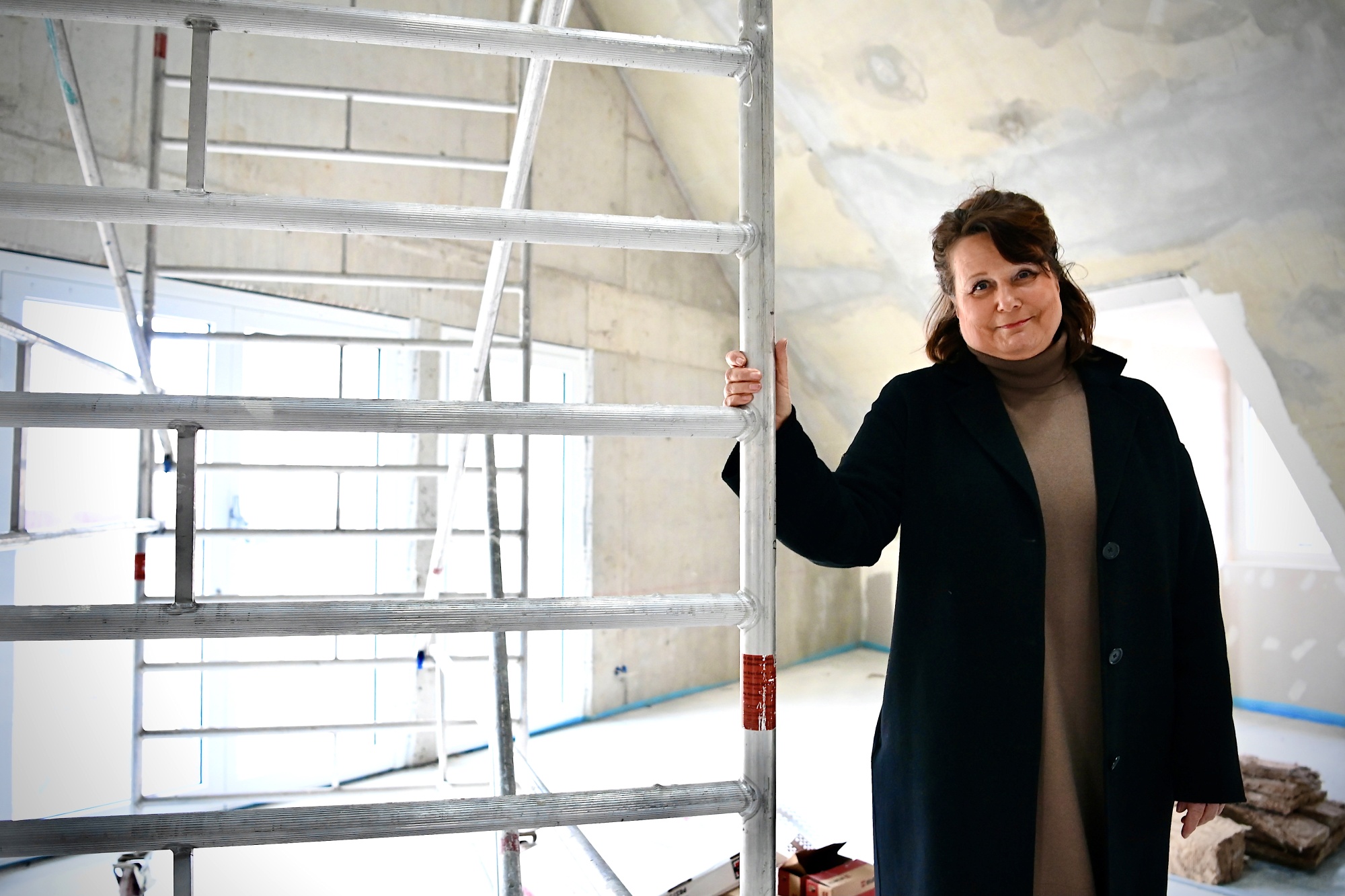 Eine Frau in schwarzer Jacke steht in einem Gebäude mit Gerüst.