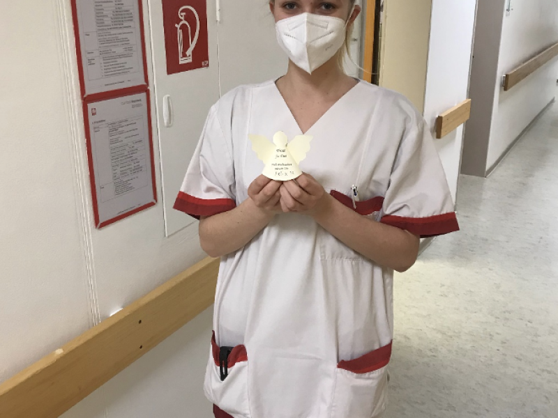 Eine Person in heller Kleidung steht in einem Flur und h&auml;lt ein Tablet oder Dokument in der Hand.
