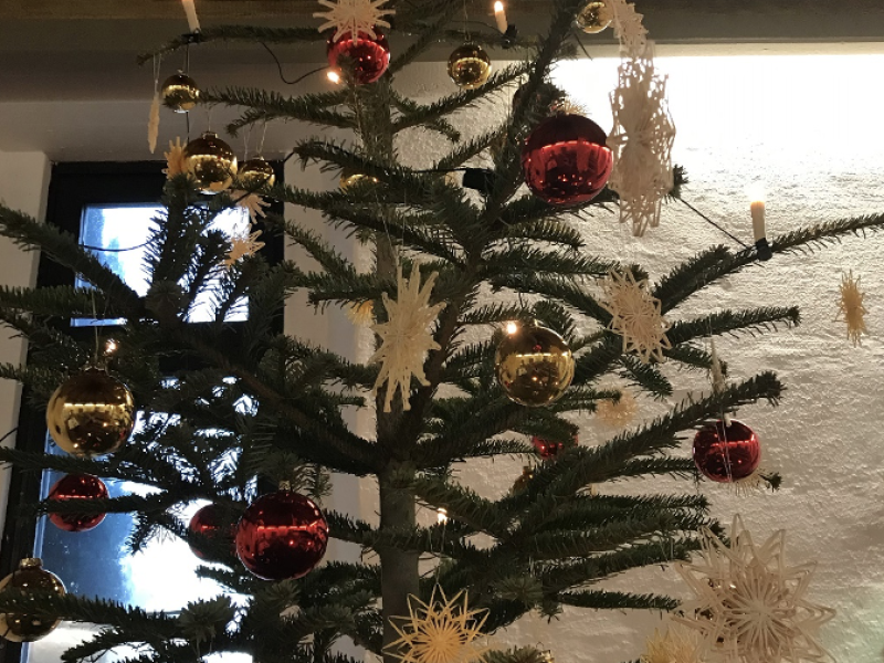 Ein geschm&uuml;ckter Weihnachtsbaum steht in einem Raum mit warmem Licht.