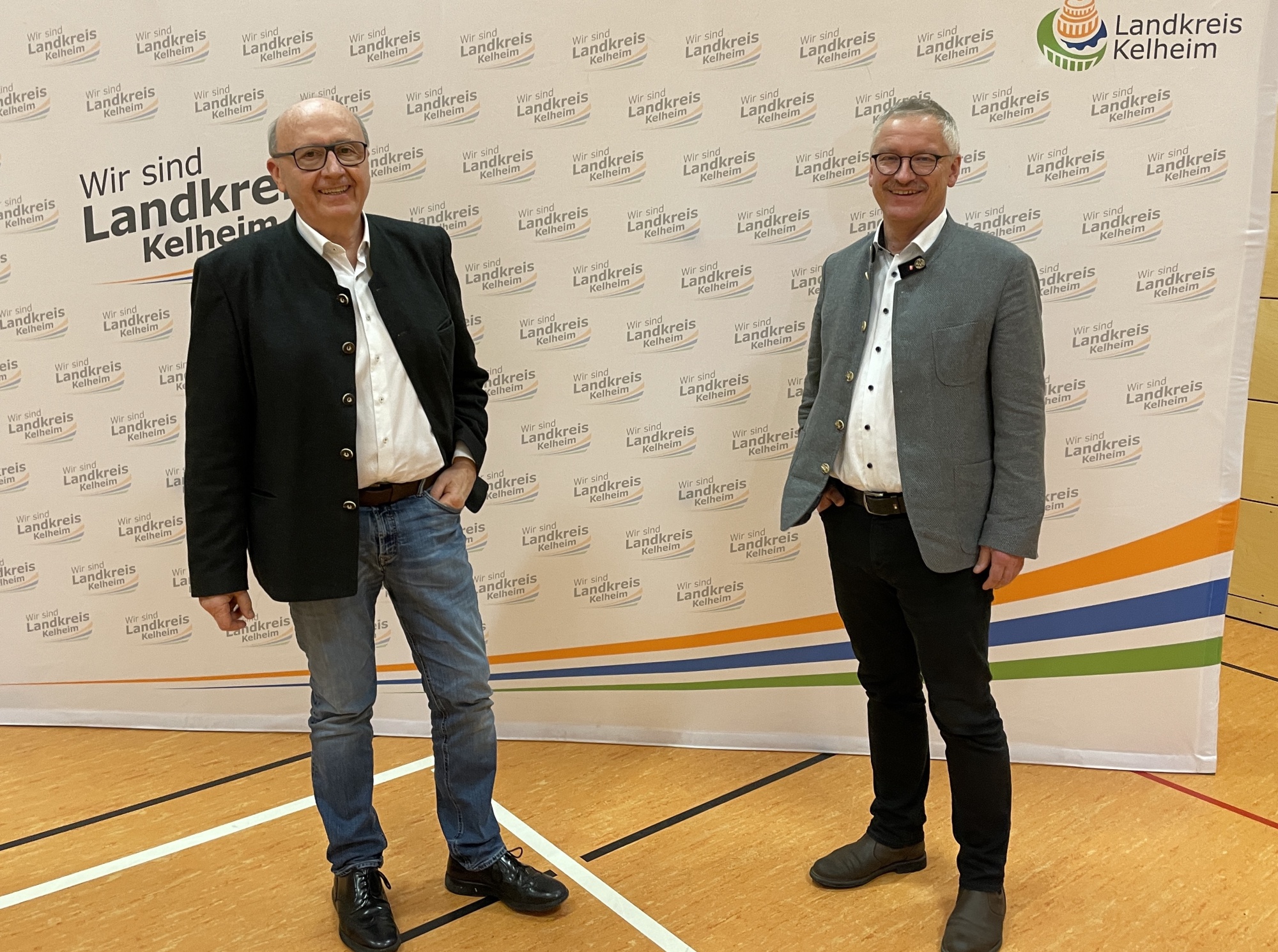 Zwei Männer stehen nebeneinander in einem Saal und sprechen miteinander.
