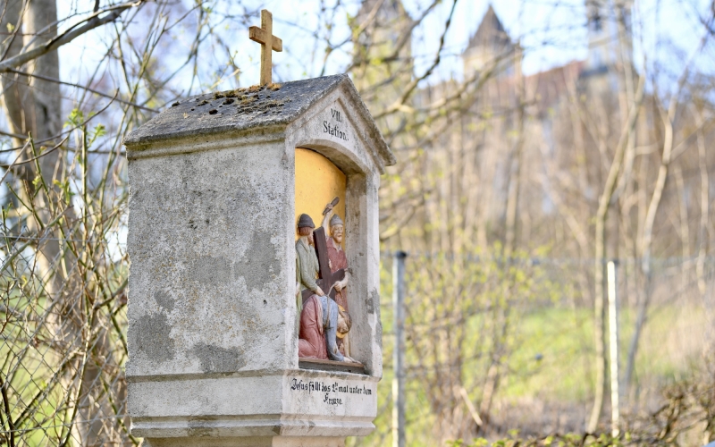 Steinkapelle mit Kreuz auf dem Dach, die die siebte Station des Kreuzwegs darstellt. Die Nische zeigt Jesus, der unter dem Kreuz zusammenbricht, umgeben von Soldaten und weinenden Frauen. Die Inschrift lautet 