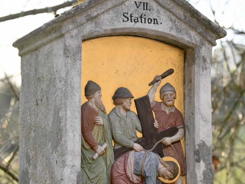Steinkapelle mit Kreuz auf dem Dach, die die siebte Station des Kreuzwegs darstellt. Die Nische zeigt Jesus, der unter dem Kreuz zusammenbricht, umgeben von Soldaten und weinenden Frauen. Die Inschrift lautet "Jesu f&auml;llt das 2te mal unter dem Kreuze.