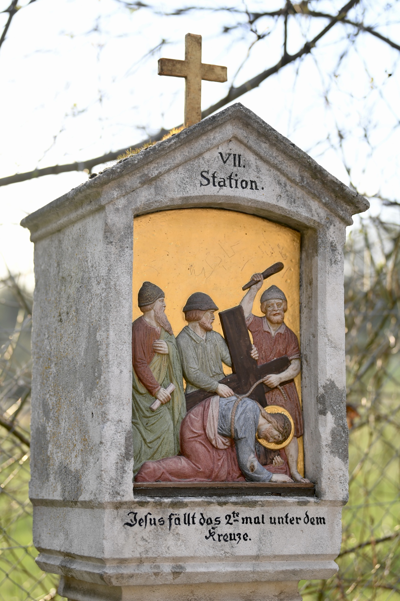 Steinkapelle mit Kreuz auf dem Dach, die die siebte Station des Kreuzwegs darstellt. Die Nische zeigt Jesus, der unter dem Kreuz zusammenbricht, umgeben von Soldaten und weinenden Frauen. Die Inschrift lautet "Jesu fällt das 2te mal unter dem Kreuze.