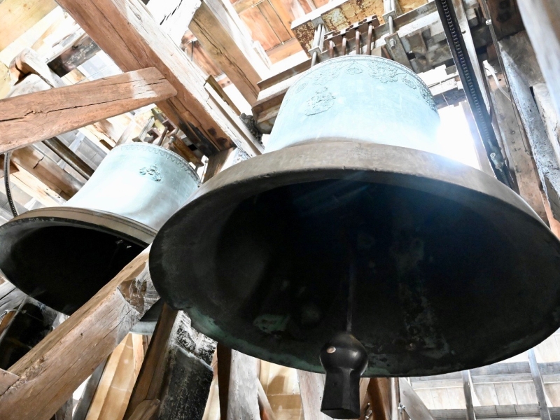 Gro&szlig;e schwarze Glocke in einem Holzger&uuml;st aufgeh&auml;ngt, daneben kleinere wei&szlig;e Glocken, Innenaufnahme eines Glockenturms oder Kirchturms.